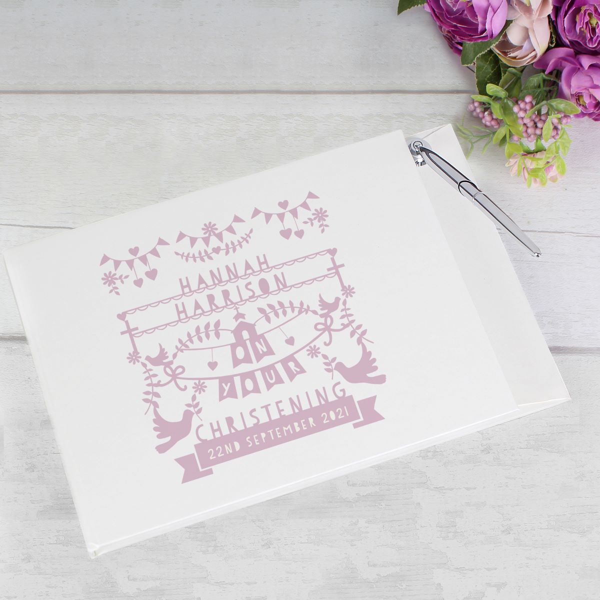 White guest book with personalized text on a light wooden surface with flowers.
