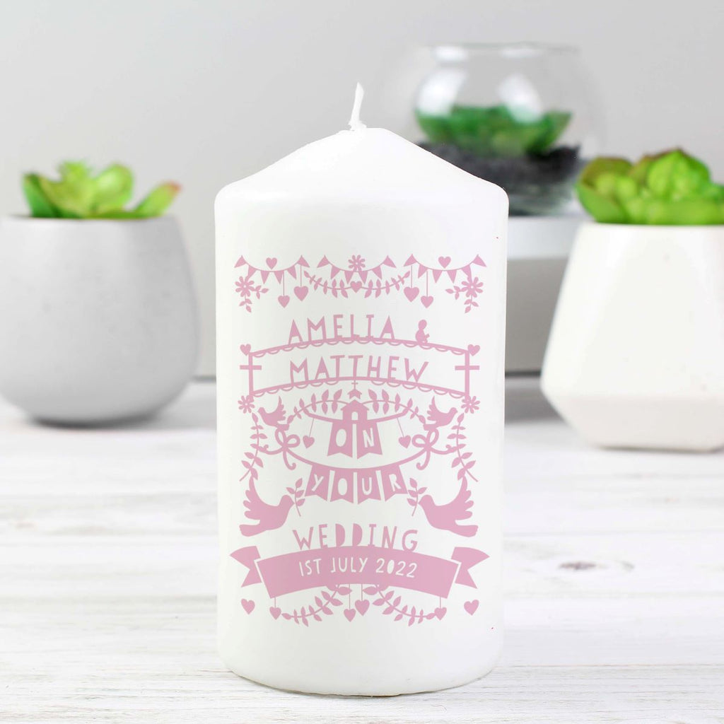 White candle with pink personalized text on a white surface with plants in the background