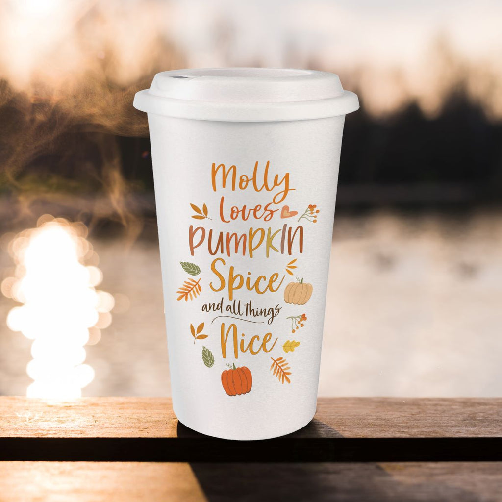 A white reusable coffee cup with a lid sits on a wooden railing outdoors. The cup has a printed autumn-themed quote reading “Molly loves Pumpkin Spice and all things Nice” in orange and brown lettering, with small pumpkins, leaves, and fall motifs.
