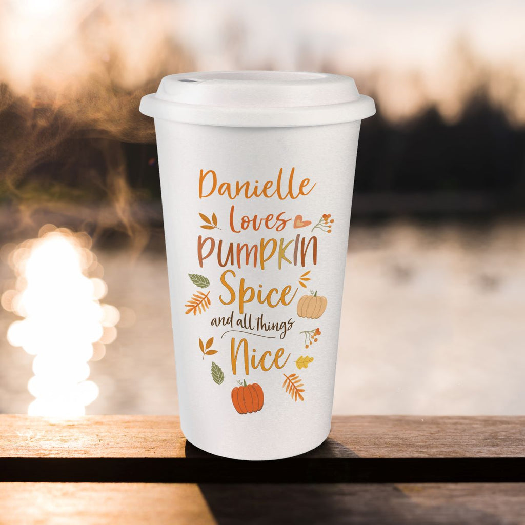 White travel mug with 'Danielle loves Pumpkin Spice and all things Nice' text on a wooden surface with blurred lights in the background.