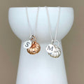 Two necklaces with initial charms on a white stand against a beige background