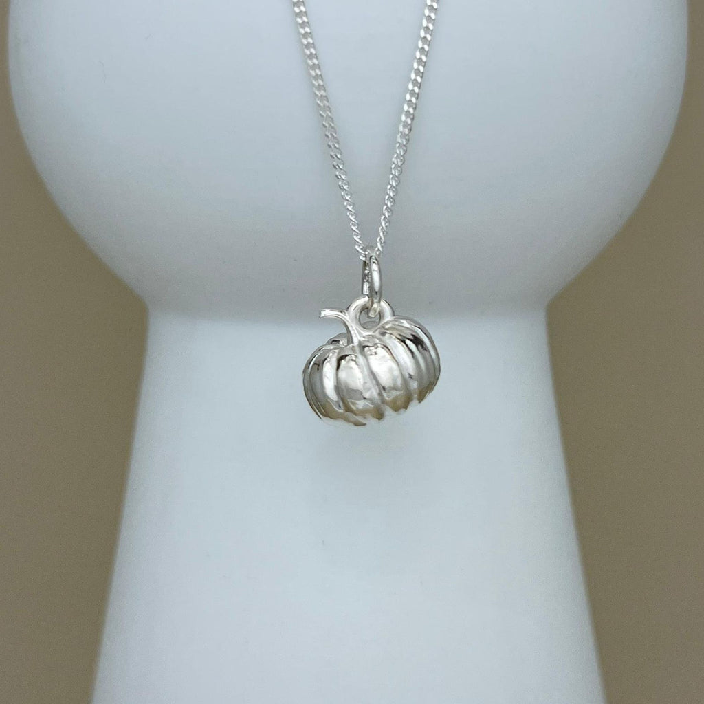 A silver pumpkin pendant necklace displayed on a white jewelry bust against a soft beige background.