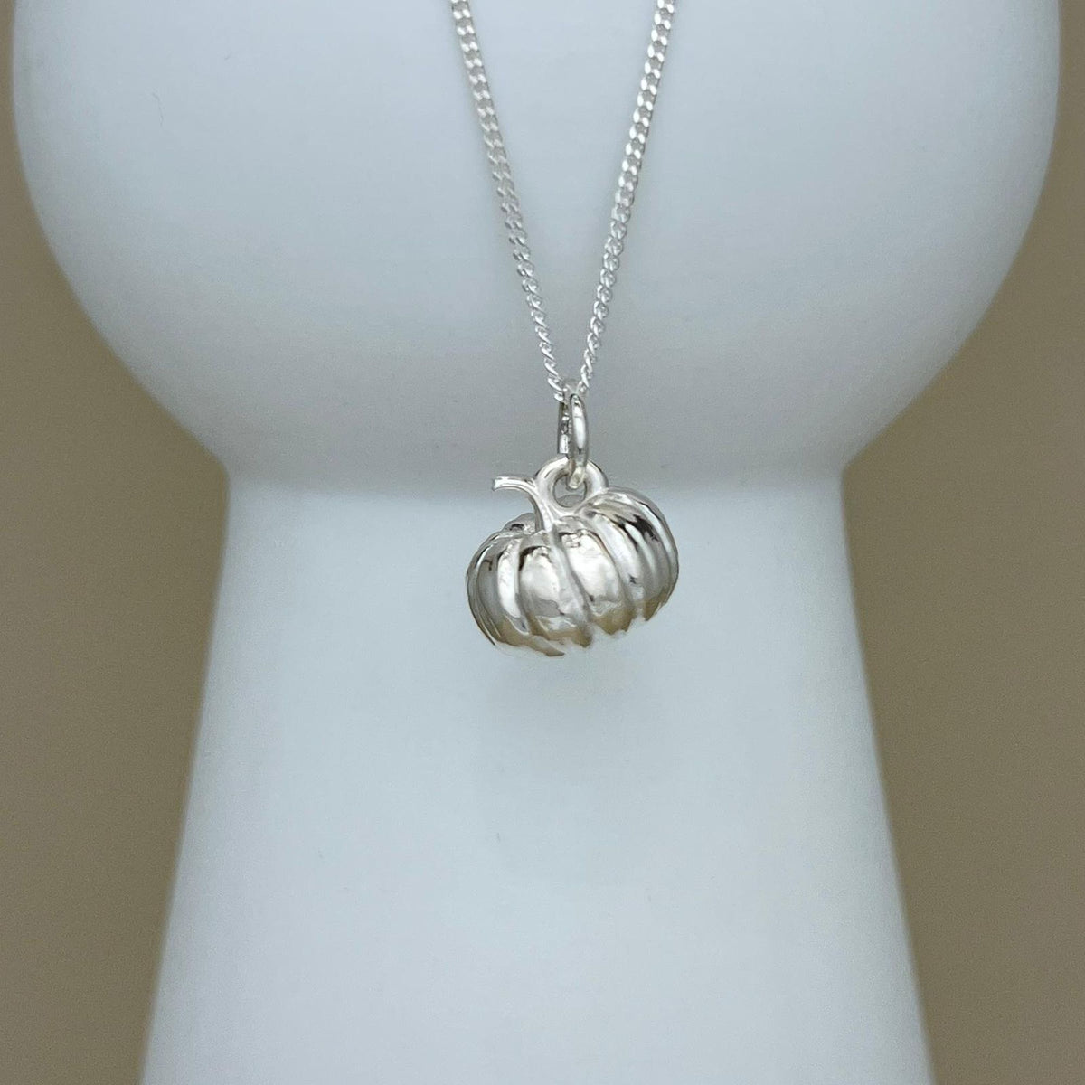 A silver pumpkin pendant necklace displayed on a white jewelry bust against a soft beige background.