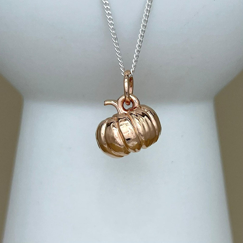 A rose gold pumpkin pendant necklace on a silver chain, displayed on a white jewelry bust.