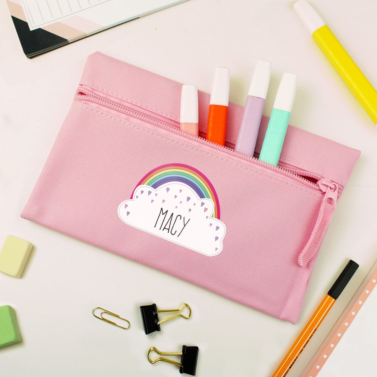 Pink pencil case with rainbow design and 'Macy' label, filled with markers, on a white background.
