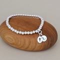 Silver beaded bracelet with charms on a wooden rock