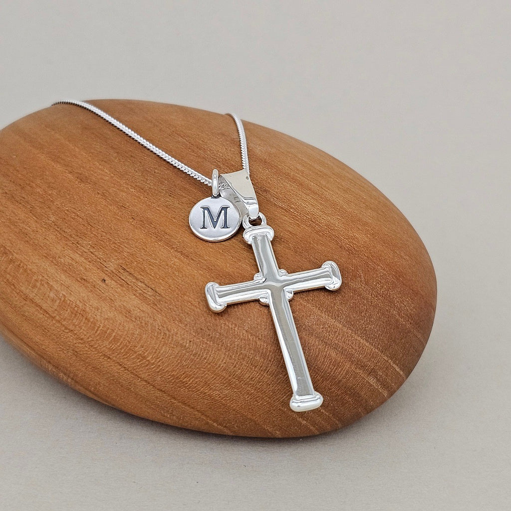 Silver cross necklace with a round pendant on a wooden rock