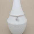 A silver beaded bracelet with a round initial 'M' charm and a star charm, displayed on a white textured cone stand against a beige background.