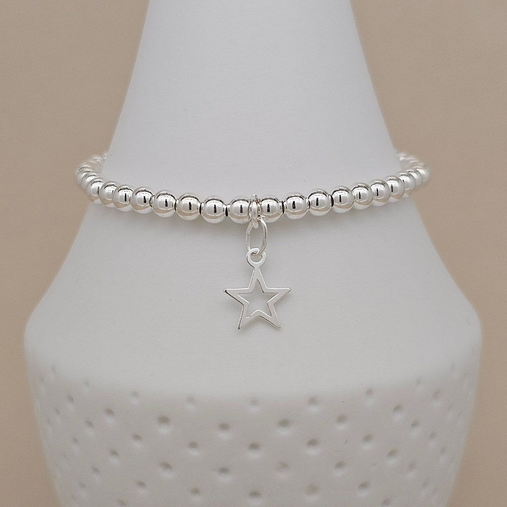 A silver beaded bracelet with a dangling open star charm, displayed on a white cone jewelry stand against a soft beige background.