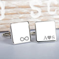 A pair of square silver cufflinks on a light grey surface. one cufflink shows an engraved infinity symbol and the other initial letters with an engraved heart symbol in the middle.