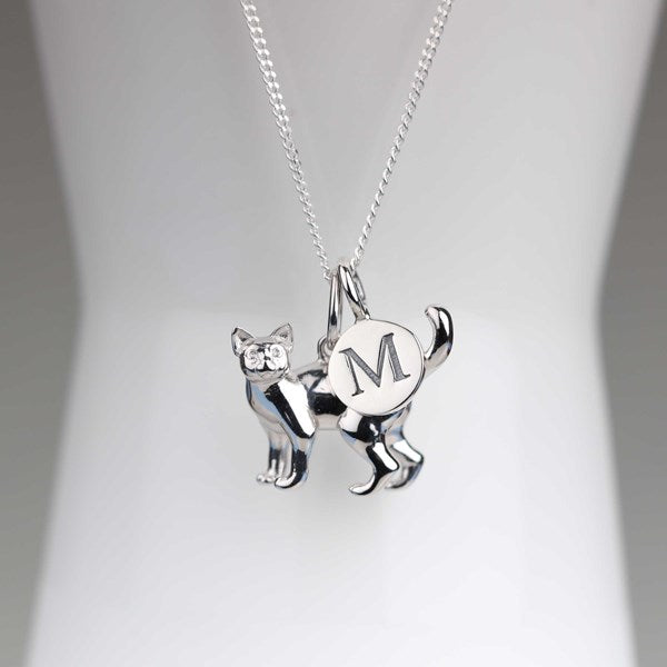 A silver necklace with a cat-shaped pendant and a circular charm engraved with the letter 'M', displayed on a white mannequin bust.