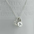 A silver necklace with a heart pendant, and a flat round disc engraved with the letter 'A', displayed against a light gray background with embossed text.