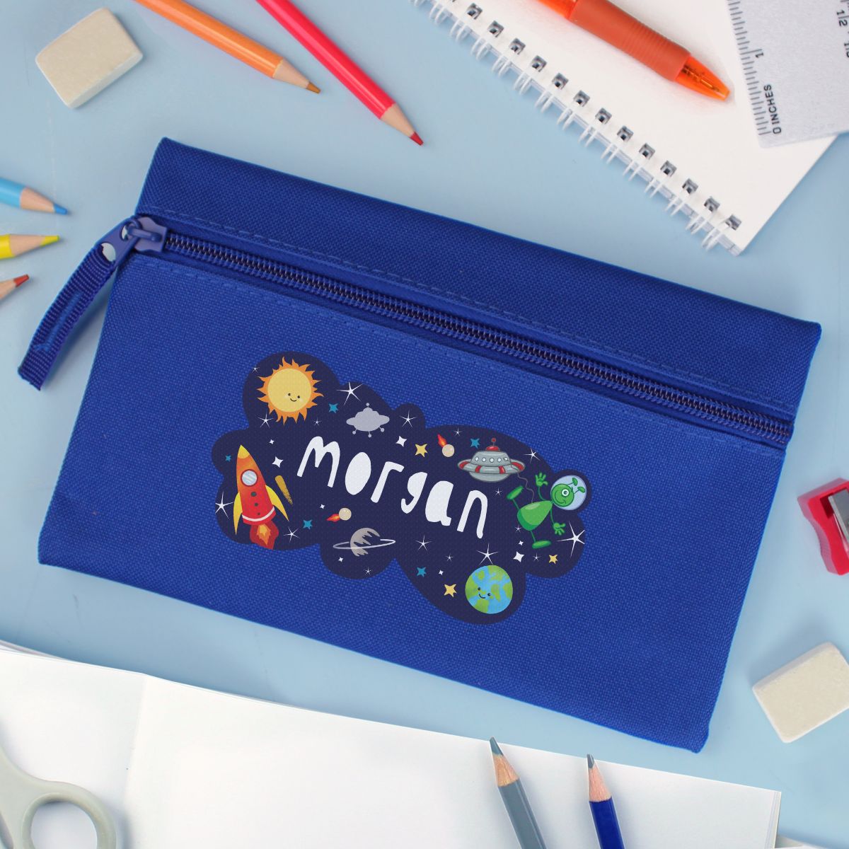 Blue pencil case with the name 'Nathan' and a space theme design on a desk with stationery items