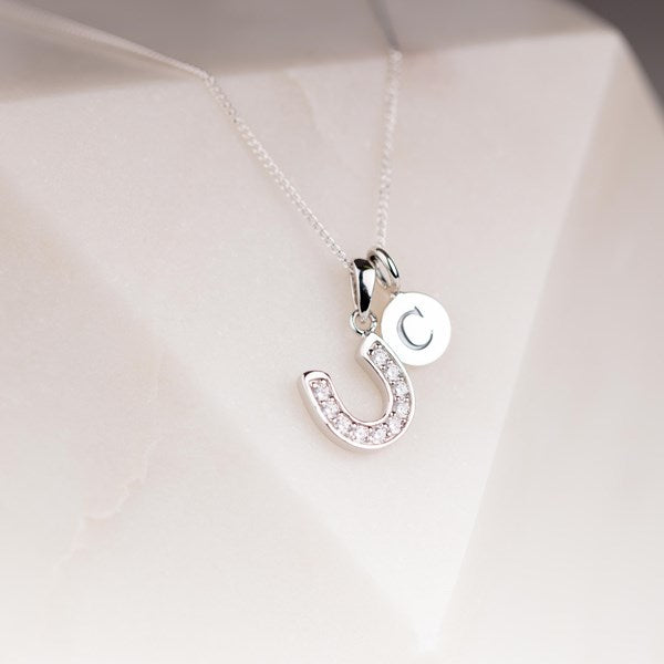 Silver horseshoe necklace with a letter 'S' pendant on a white background