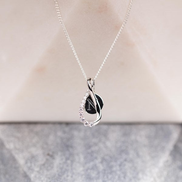 A silver pendant necklace featuring a letter charm and a teardrop-shaped silver frame partially encrusted with small clear stones, displayed on a neutral background.