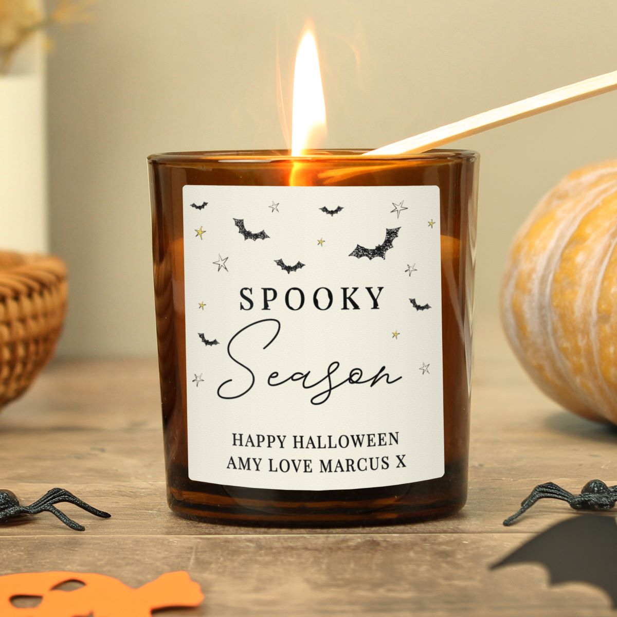 Candle with a 'Spooky Season' label on a wooden surface with Halloween decorations.