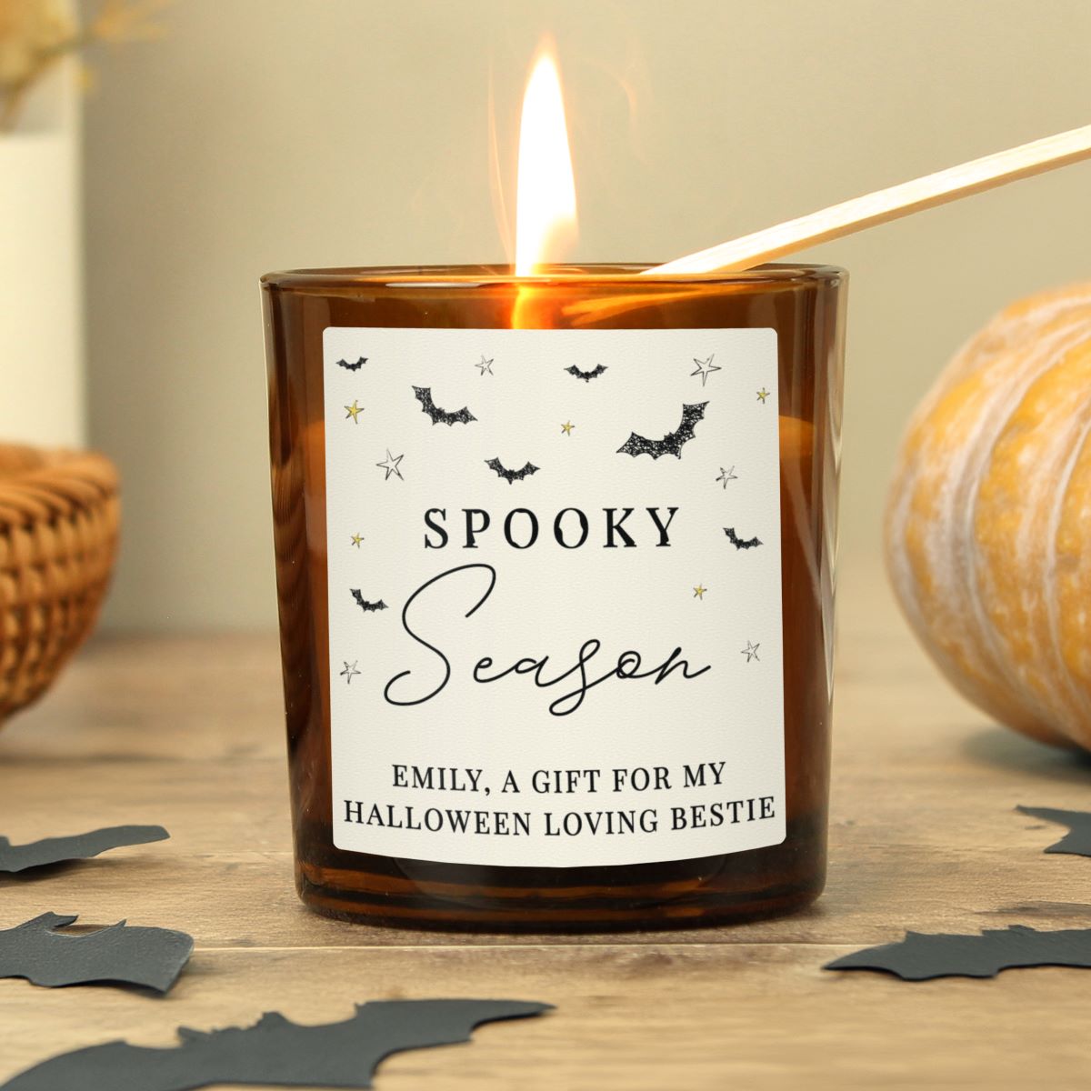 Candle with a 'Spooky Season' label on a wooden surface with Halloween decorations.