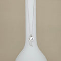 A silver necklace with a wing and round initial pendant displaying the letter 'J', displayed on a white ceramic vase against a beige background.