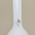 A silver ballerina pendant necklace with a small circular initial 'C' charm, displayed on a white ceramic stand against a neutral beige background.