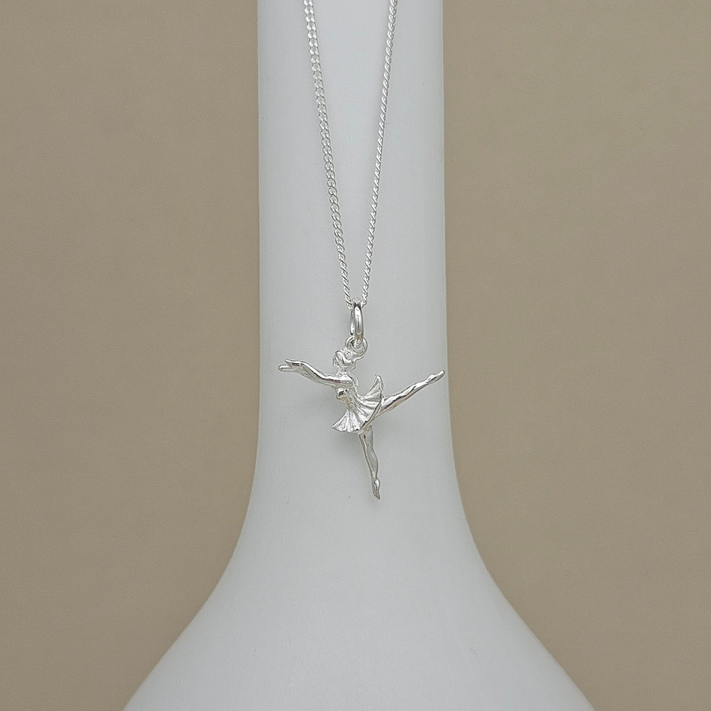 A silver ballerina pendant necklace displayed on a white neck mannequin against a solid beige background.