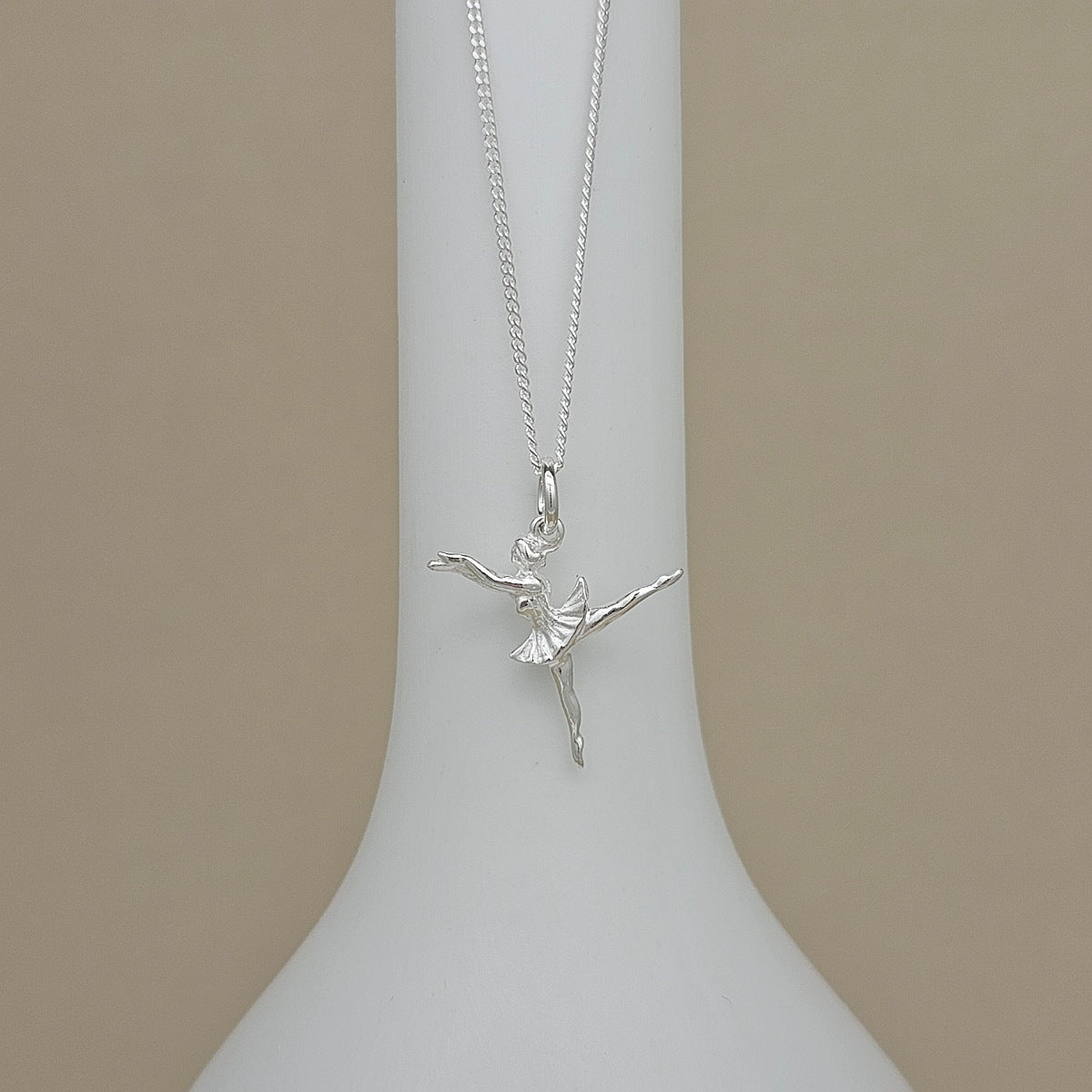 A silver ballerina pendant necklace displayed on a white neck mannequin against a solid beige background.