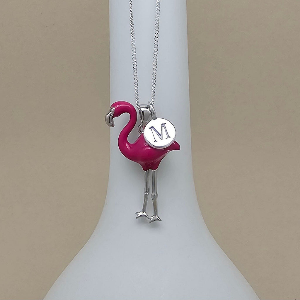 Flamingo-shaped pendant with a letter 'M' on a white stand against a beige background