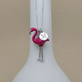 Flamingo-shaped pendant with a letter 'M' on a white stand against a beige background
