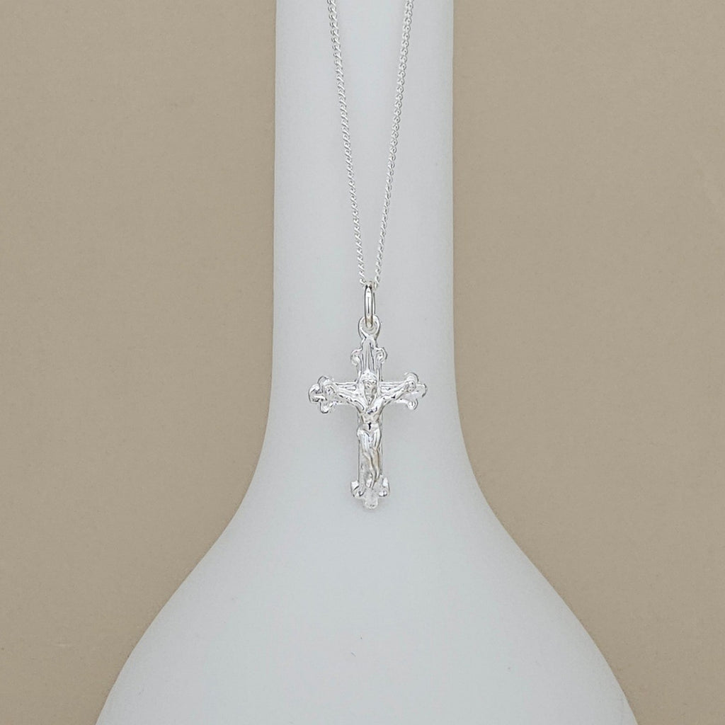 A silver crucifix pendant necklace displayed on a white neck mannequin against a solid beige background.