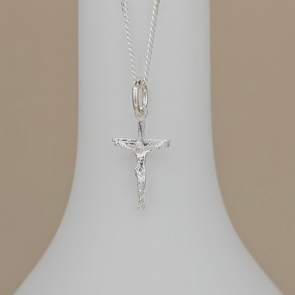 A silver crucifix pendant necklace displayed on a white jewelry bust against a soft beige background.
