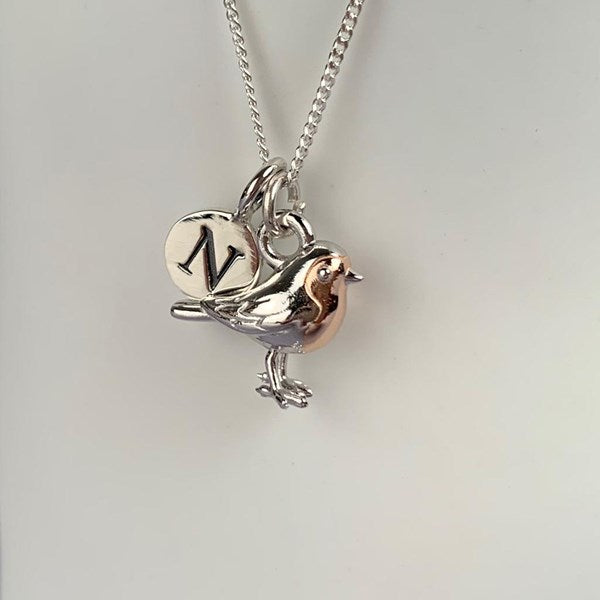 Silver bird-shaped pendant with a rose gold accent and 'N' charm on a chain against a light gray background.