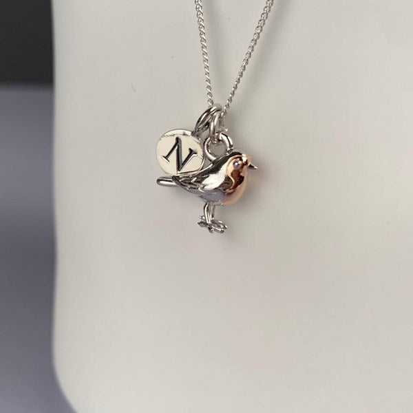 A silver necklace with a bird charm and a round engraved disc pendant, displayed on a white mannequin bust.