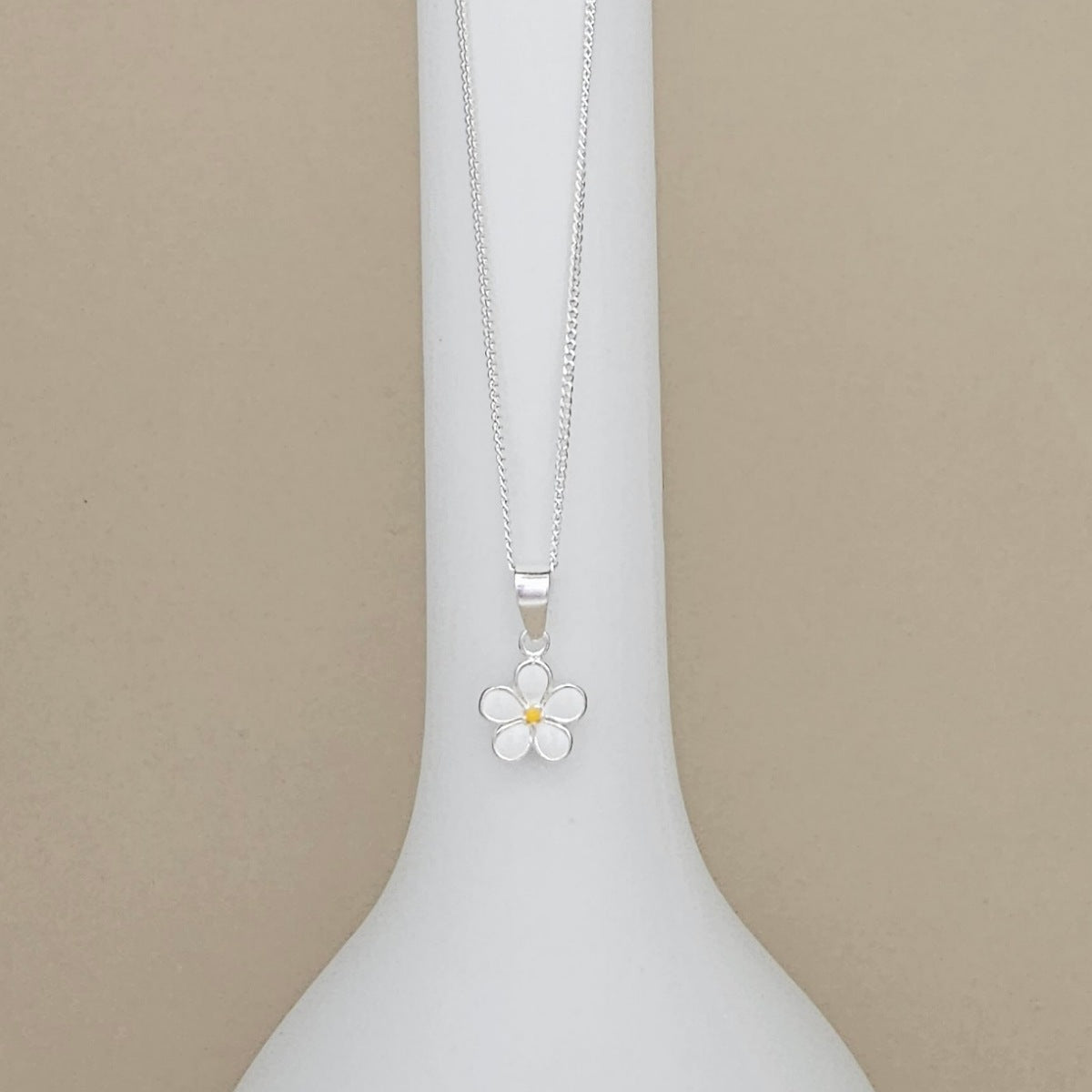 A silver flower pendant necklace with a small yellow center, displayed on a white neck mannequin against a beige background.