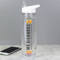 A clear plastic water bottle with a white flip-top lid, featuring a vertical printed design that reads 'MR RICHARDS WORLD'S BEST TEACHER' with two yellow pencils. A smartphone lies on a light marble surface in the background against a gray wall.