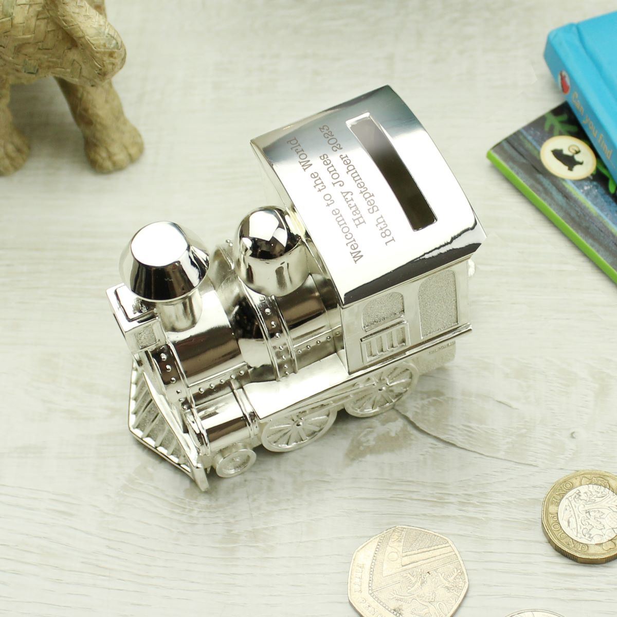 Silver train-shaped money box on a light surface with coins around it