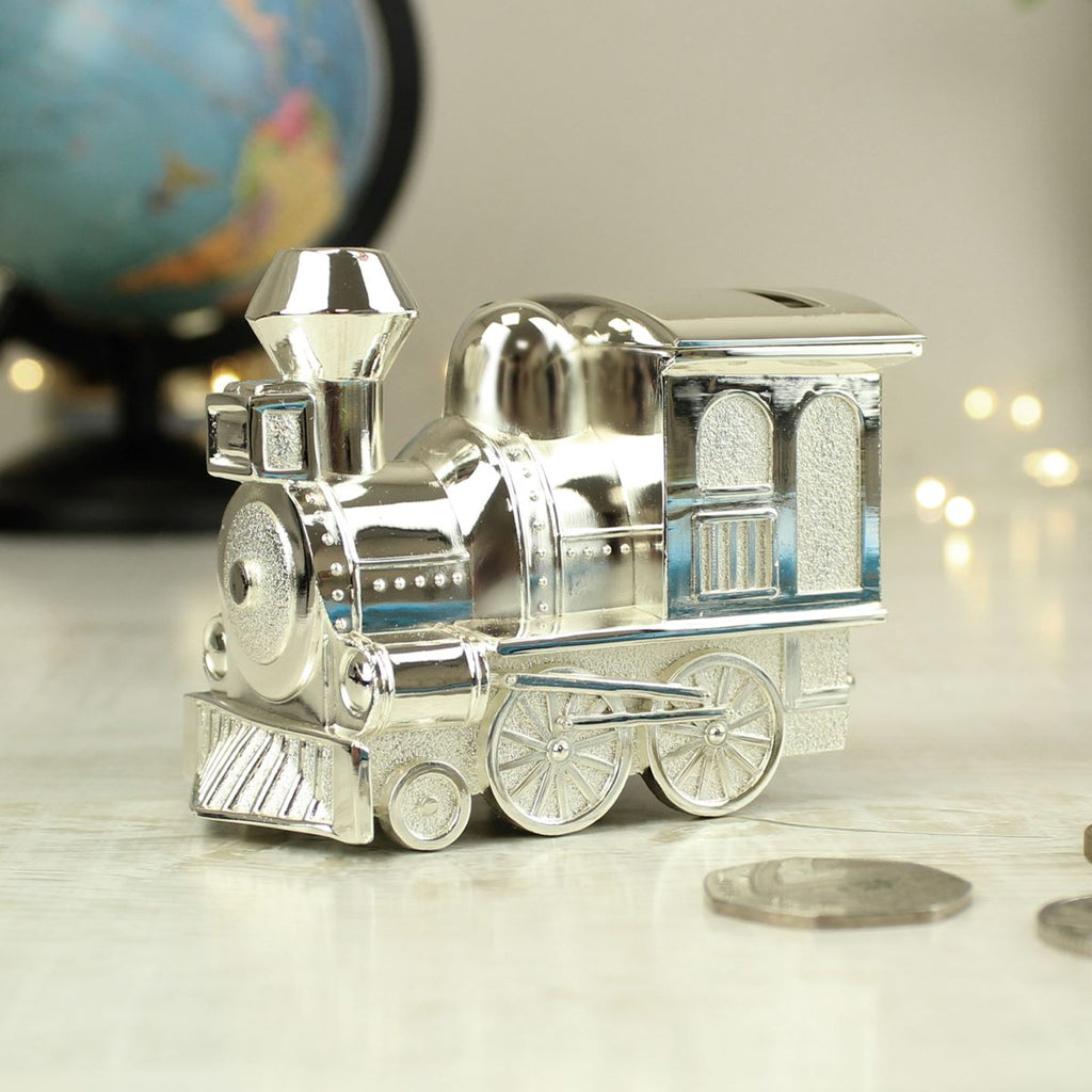 Silver toy train moneybox on a reflective surface with a blurred globe in the background