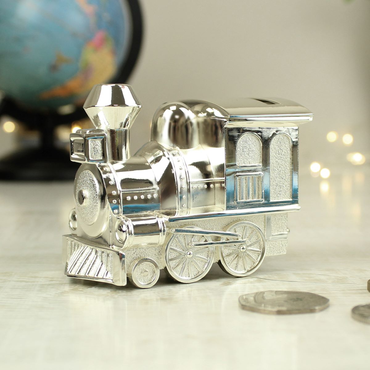 Silver toy train moneybox on a reflective surface with a blurred globe in the background