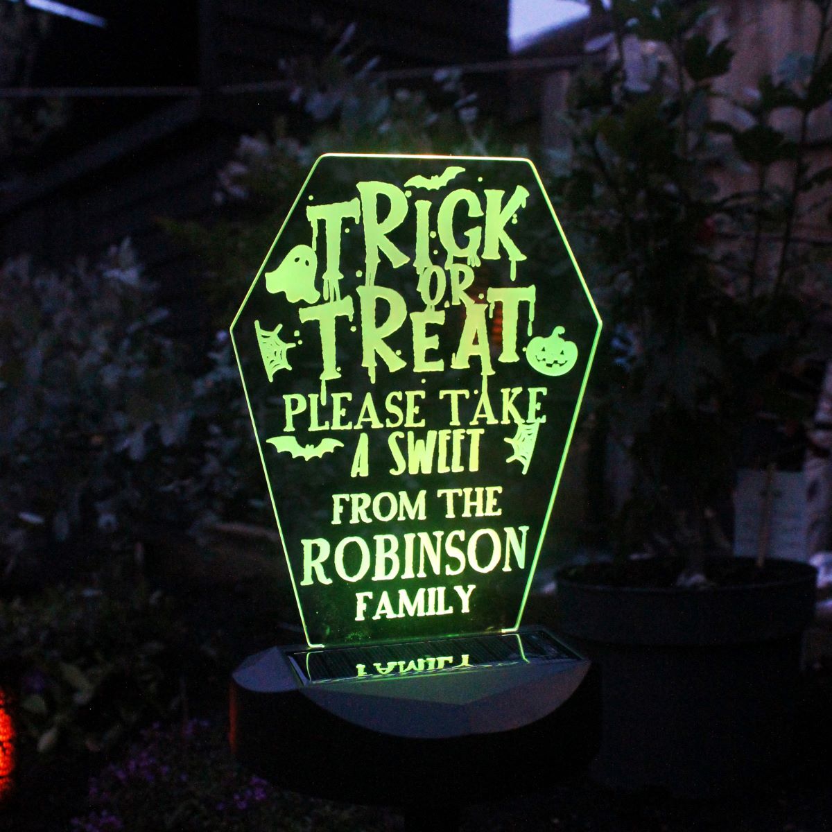Glowing Halloween-themed sign with personalized text in a dark outdoor setting.