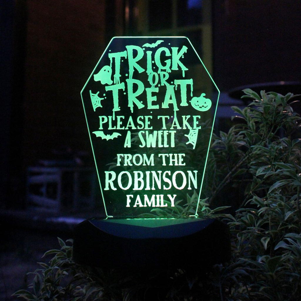 Halloween-themed decorative sign with text 'Trick or Treat, please take a sweet from the Robinson family' on a dark background.