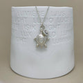 A sterling silver turtle pendant necklace with a letter charm, displayed on a white ceramic candle holder against a neutral beige background.