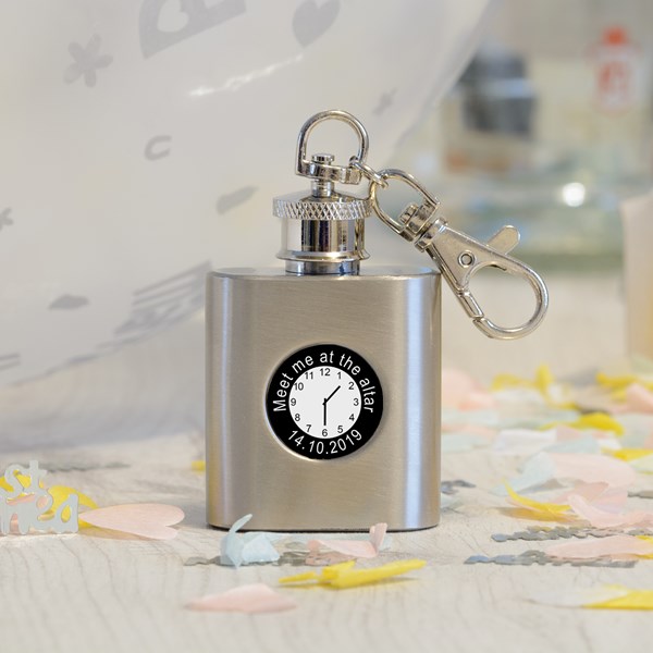 Silver flask with keychain and personalised clock sticker with a time and the wording 'Meet me at the alter 14.10.2019' on a decorative surface