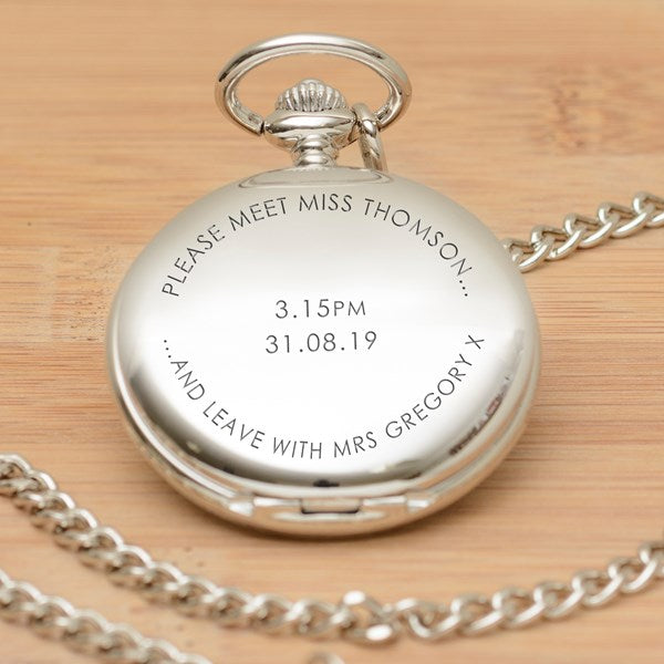 A silver pocket watch pendant with a matching chain, engraved with the wording 'PLEASE MEET MISS THOMSON....... AND LEAVE WITH MRS GREGORY X' and the time and date in the centre, displayed on a light wood background.