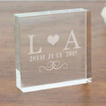 Clear glass block with engraved initials 'L' and 'A', date '28th July 2015', and heart symbol on a wooden surface.