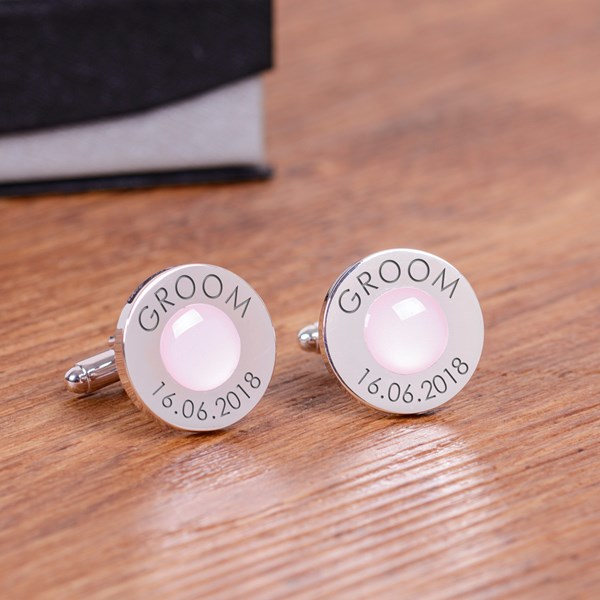 A pair of round personalised silver cufflinks with a light pink circular gem centre and engraved text reading 'GROOM' and '16.06.2018'.