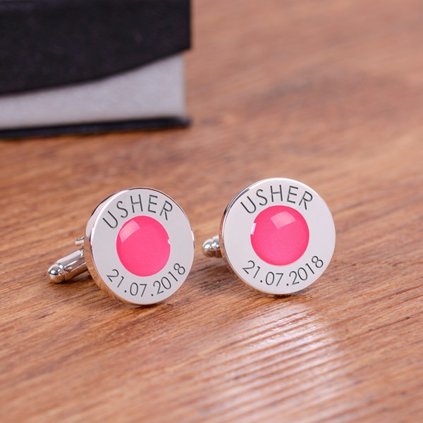 A pair of round personalised silver cufflinks with a bright pink circular gem centre and engraved text reading 'USHER' and '21.07.2018'.