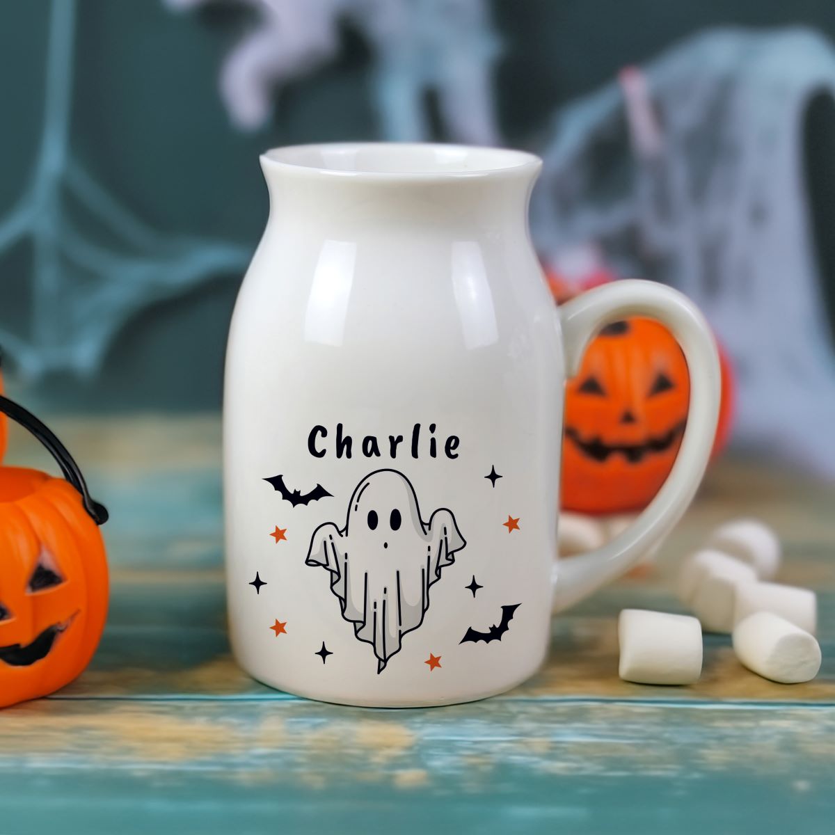 White ceramic mug with ghost design and 'Charlie' text, surrounded by Halloween decorations.