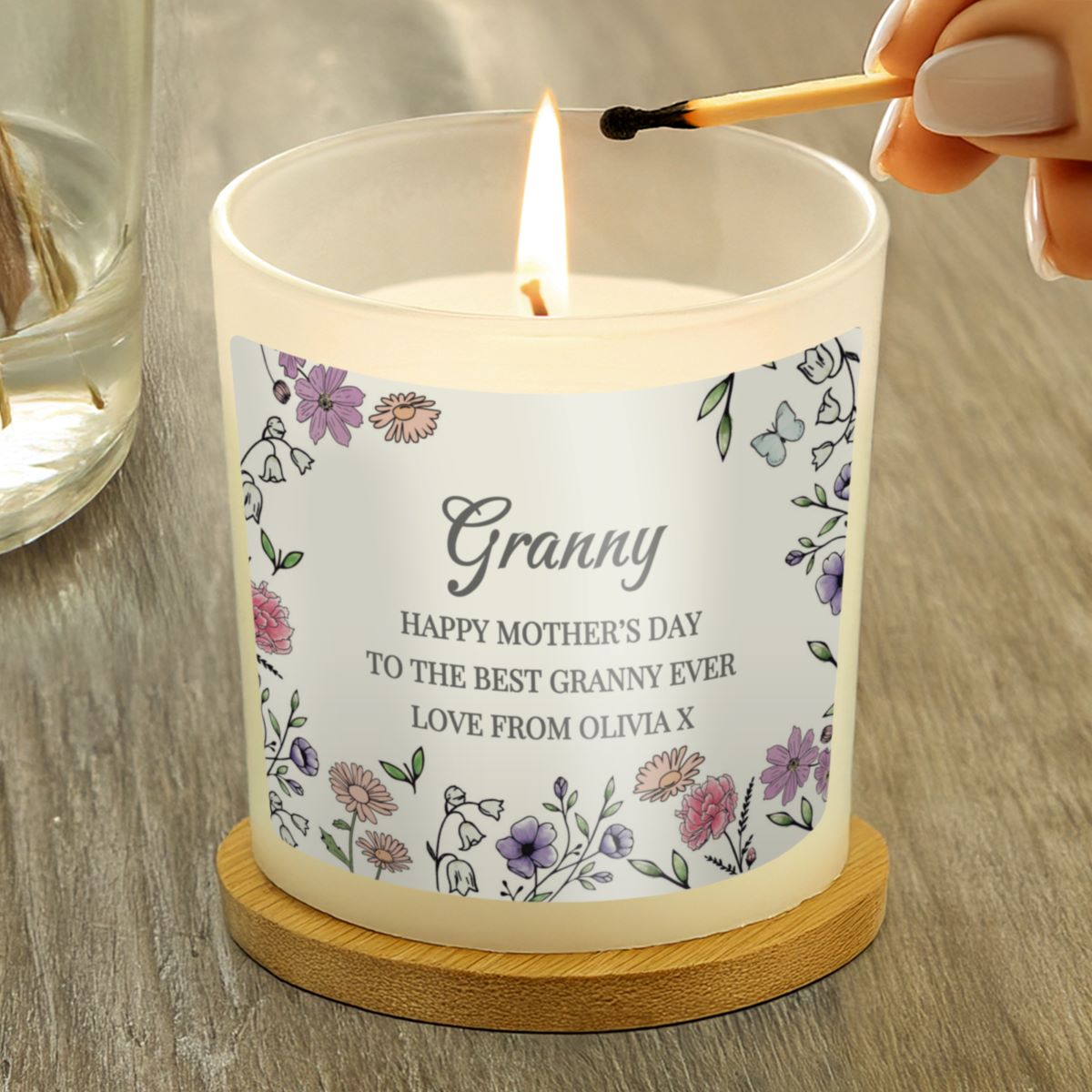 Candle with a personalized label being lit on a wooden surface