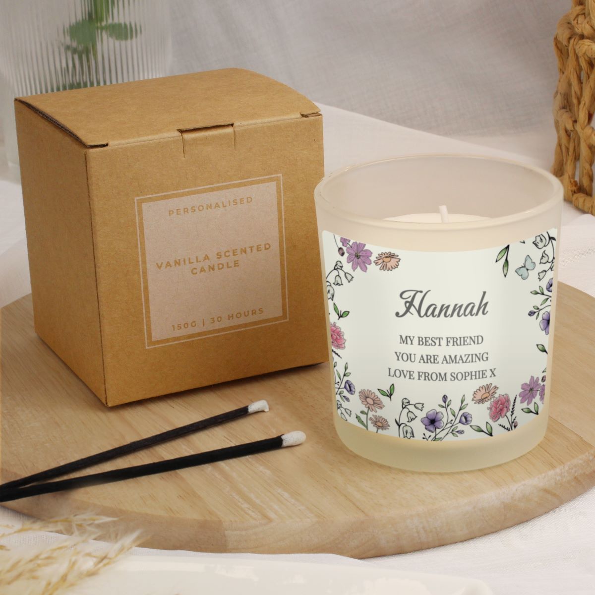 Personalized vanilla scented candle with floral label and packaging on a wooden surface.