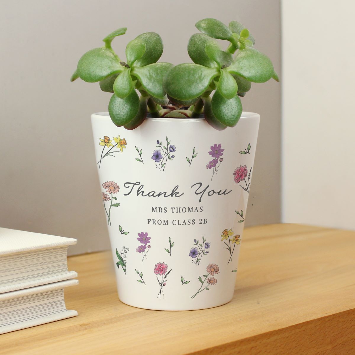 White pot with floral designs and a plant on a wooden surface