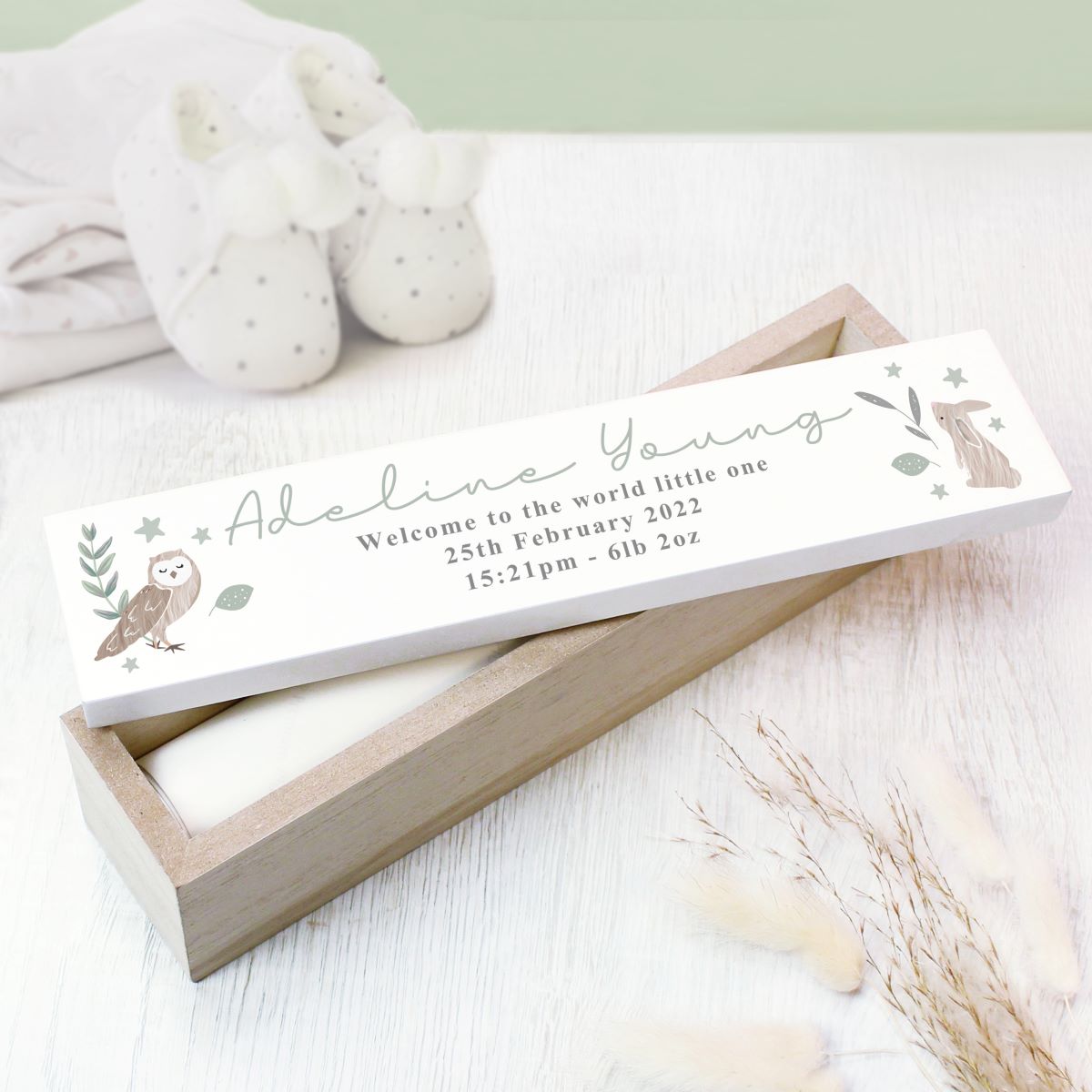 Wooden box with a birth announcement card featuring an owl design on a light wooden surface.