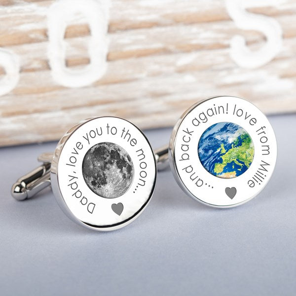 A pair of round silver cufflinks displayed on a light grey surface. One cufflink features a detailed engraving of the moon with the text 'Daddy, love you to the moon...'  and the other cufflink features a map of the world with the text '... and back again! love from Millie.